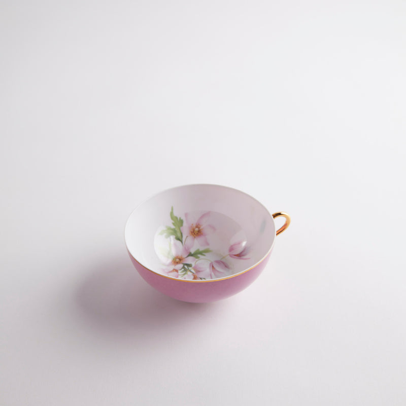 Pink tea cup with gold handle and floral design inside.