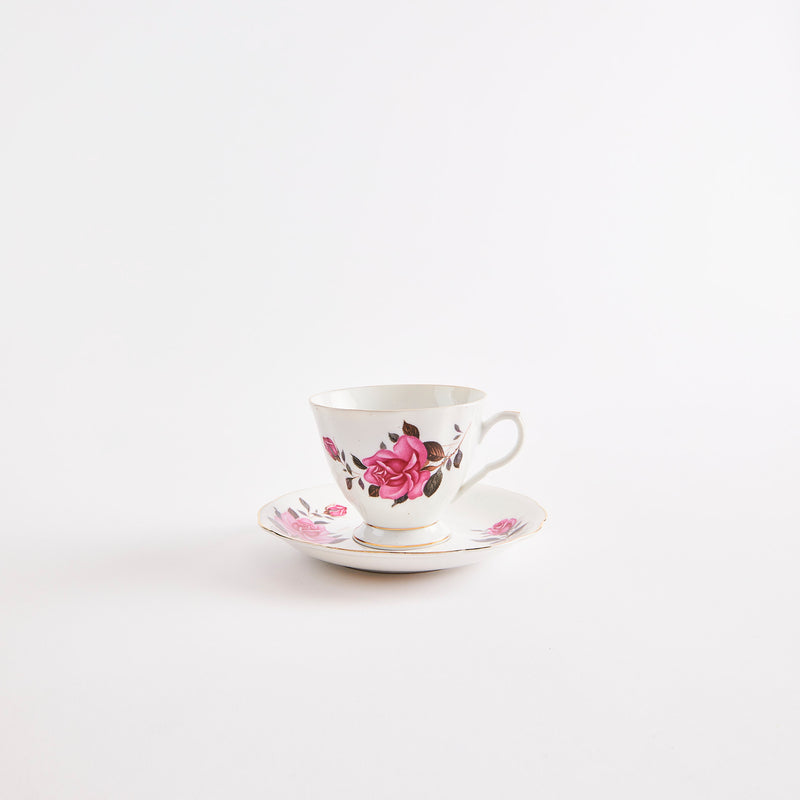 White teacup and saucer with gold rim & pink floral pattern.
