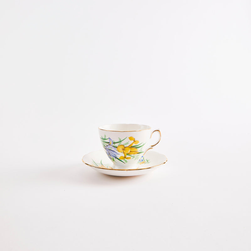 White teacup and saucer with gold rim & yellow and blue floral pattern.