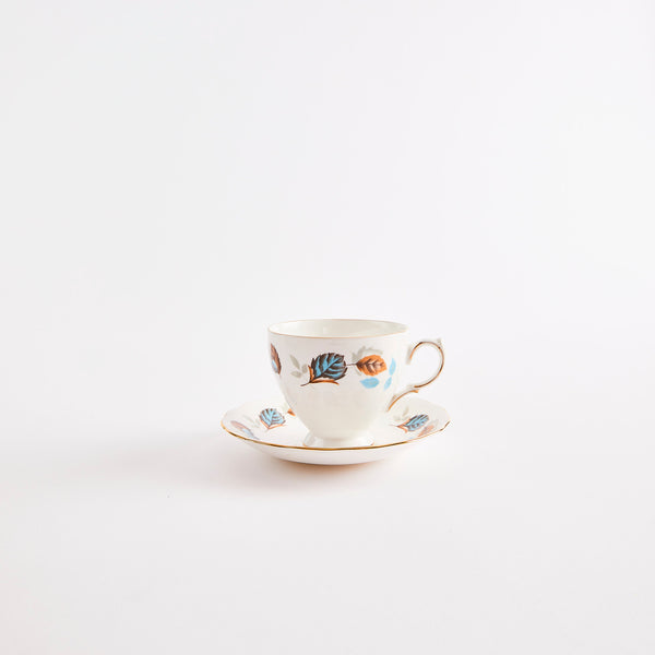 White teacup and saucer with gold rim & blue and orange leaf pattern.