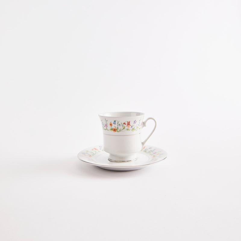 White teacup and saucer with silver rim and mulitcolour floral design.