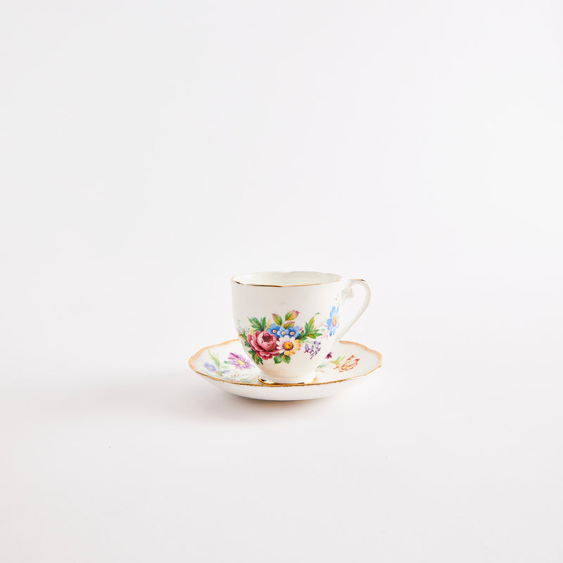 White teacup and saucer with gold rim and multicolour floral design.