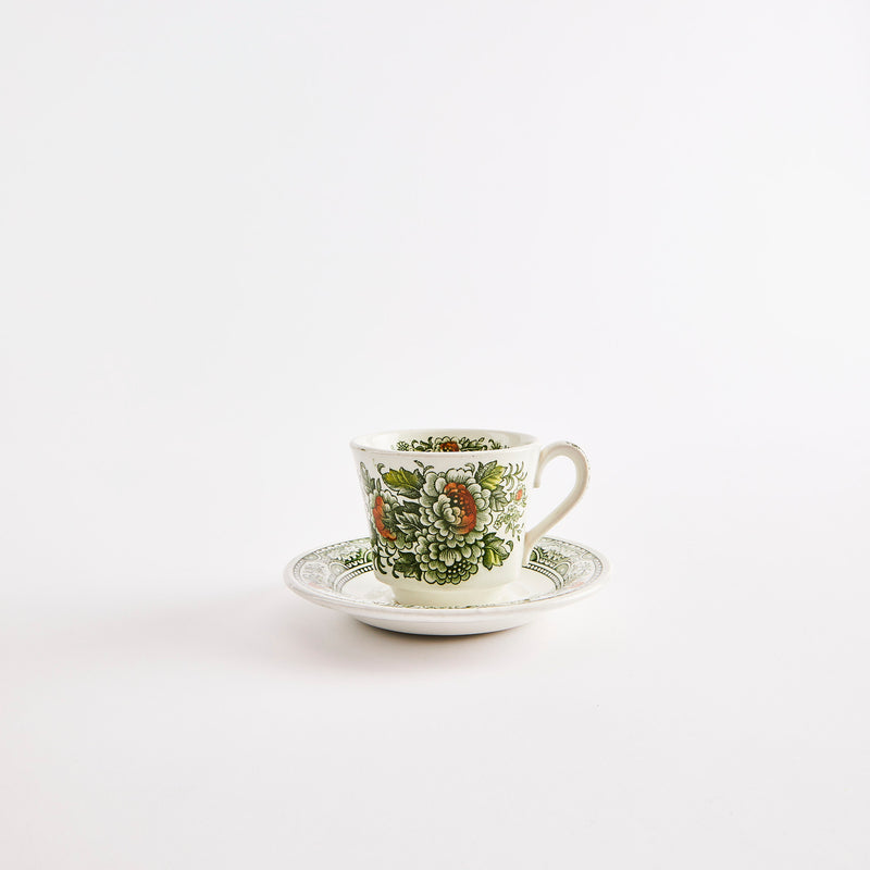 White teacup and saucer with green floral print.
