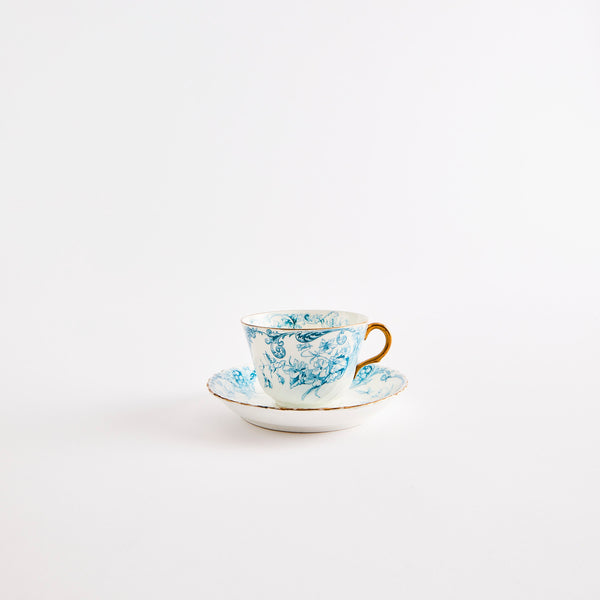 White and blue intricate design teacup and saucer with gold rim.