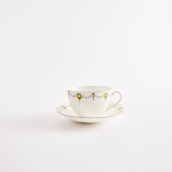 White teacup and saucer with floral design and gold rim.