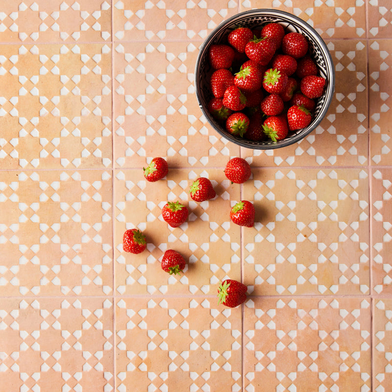 Top view of bowl full of strawberries with mixed white and orange tiled background.