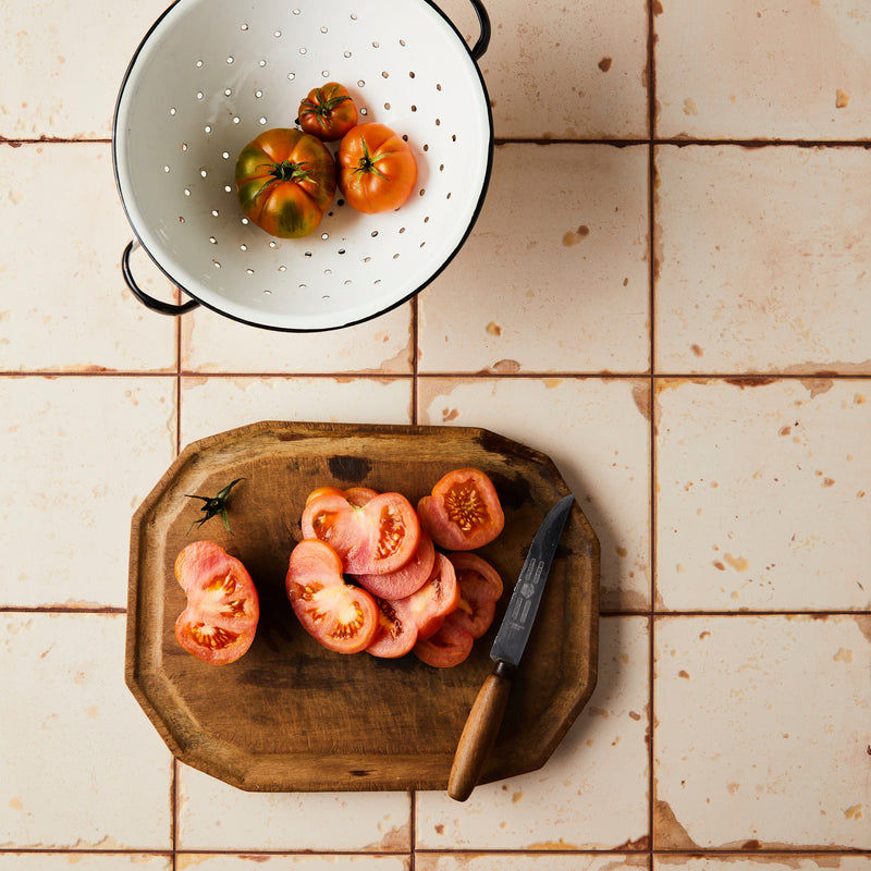 Top view of tomatoes and slices on cutting board with Orange and cream tile background.