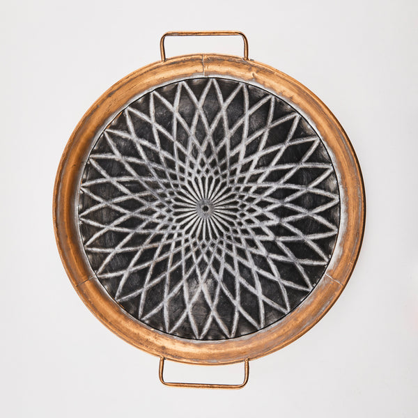 Black and copper circular tray with worn embossed design.
